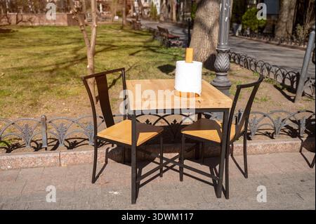 Table en bois vide avec des serviettes blanches dans un support en métal dans un café en plein air. Concept de préparation du restaurant, heure du café du matin, et urbain paisible Banque D'Images
