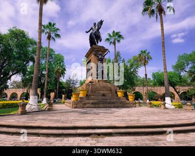 Une statue d'un homme à cheval se dresse devant un grand bâtiment. La statue est entourée de palmiers et de plantes en pot. La scène est paisible Banque D'Images
