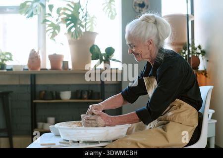 Femme senior Shaping Clay pot sur la roue de poterie dans Art Studio Banque D'Images