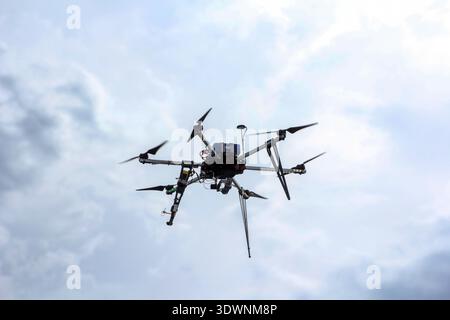 Drone Hexacopter à six rotors volant contre un ciel nuageux. Véhicule aérien sans pilote moderne à hélices multiples en vol. Technologie et aviatio Banque D'Images