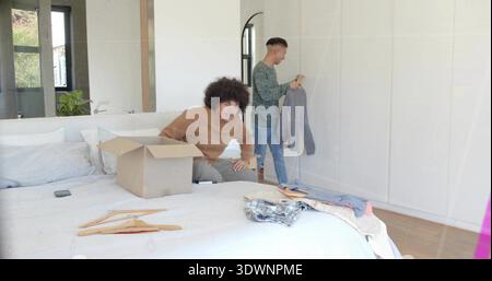 Tri de deux hommes dans des vêtements décontractés déballage des vêtements sur le lit dans la chambre, avec boîte en carton ouverte Banque D'Images