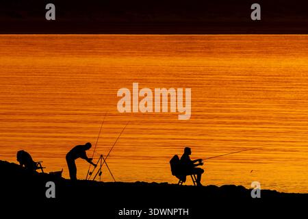 Silhouette de deux pêcheurs récréatifs / pêcheurs avec plusieurs cannes à pêche à la ligne au coucher du soleil Banque D'Images