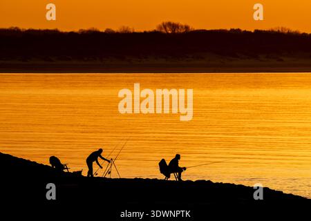 Silhouette de deux pêcheurs récréatifs / pêcheurs avec plusieurs cannes à pêche à la ligne au coucher du soleil Banque D'Images
