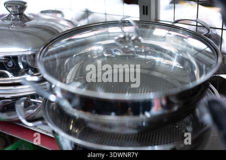 Casseroles en acier inoxydable avec couvercles en verre affichés dans un étal de marché, scène d'ustensiles de cuisine urbains Banque D'Images