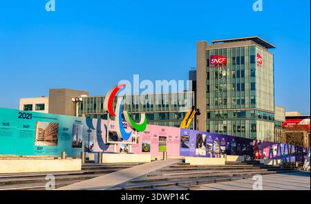 Saint-Denis, France - 29 décembre 2025 : vue panoramique ensoleillée sur le monument paralympique d'Agitos, une réserve de timeline colorée et le bâtiment moderne en verre du siège du Groupe SNCF près de Paris. Banque D'Images