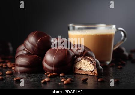 Biscuits soufflés au café enrobés de chocolat. Dessert au chocolat et tasse de café à la crème sur une table noire. Banque D'Images