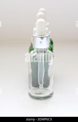 Flacons compte-gouttes en verre vert et transparent vides sur une table blanche avec fond blanc, idéaux pour les cosmétiques, les soins de la peau, l'huile essentielle ou la pharmaceutica Banque D'Images