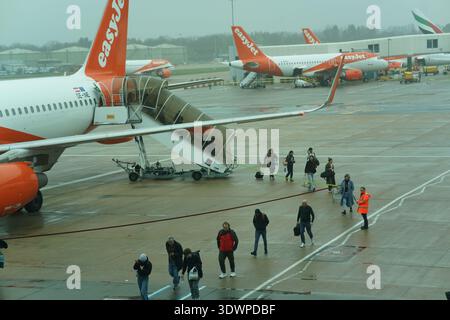 Passagers débarquant de l'easyJet Airbus par des escaliers ouverts sur un tablier humide pluvieux à l'aéroport de Londres Gatwick, équipage au sol à proximité, aviation britannique. Banque D'Images