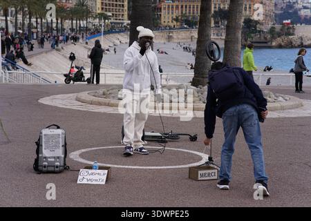 Distributeur automatique vintage placé devant une grande affiche en noir et blanc représentant une plage bondée de Nice, en France, créant un contraste urbain saisissant. Banque D'Images