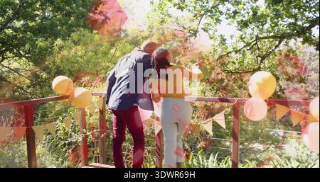 Couple penché regardant la vue boisée de la terrasse décorée, avec des ballons, femme en haut jaune Banque D'Images