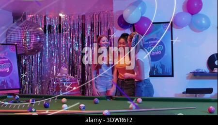 Souriant trois femmes portant des hauts rouges, orange, blancs avec du denim à la table de billard, boule disco Banque D'Images