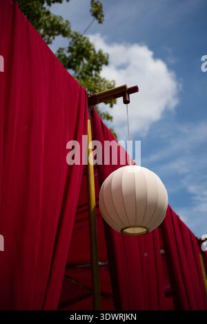 Installations colorées de lanternes décoratives suspendues au-dessus d'une rue dans une ancienne ville photographiée sous un angle bas contre le ciel bleu et les nuages. Banque D'Images
