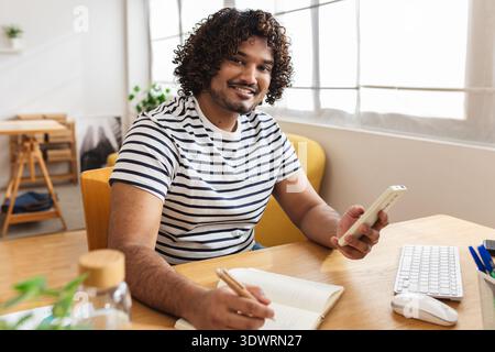 Jeune homme indien souriant tout en utilisant un smartphone Banque D'Images