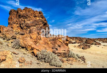 Vue panoramique ensoleillée sur de grandes formations rocheuses volcaniques brun rougeâtre et des arbustes du désert dans le paysage ponce de Minas de San Jose dans le parc national du Teide, Tenerife. Banque D'Images