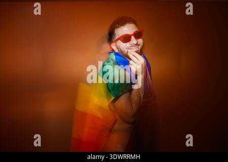Homme heureux portant des lunettes de soleil rouges et une cape drapeau arc-en-ciel célébrant sa fierté Banque D'Images