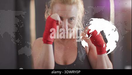 Boxer de femme de formation levant les poings dans le gymnase, portant un réservoir sombre et des enveloppements de main rouges, carte ou globe overla Banque D'Images