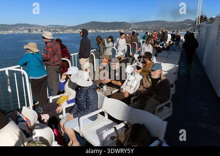 Passagers sur le pont du ferry Interislander au départ de Wellington, Nouvelle-Zélande, avec les collines côtières et l'eau bleue en vue. Banque D'Images