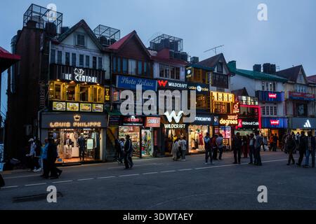 Les piétons passent devant les vitrines illuminées et les restaurants le long de la célèbre Mall Road à Shimla pendant la soirée. Banque D'Images
