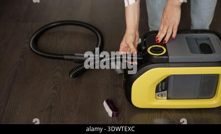 Une femme avec une manucure rouge assemble un aspirateur jaune et noir, connectant le tuyau avant le nettoyage. Mode de vie photo des tâches domestiques sur un d Banque D'Images
