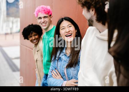 Jeunes amis divers souriant et discutant près du mur à l'extérieur Banque D'Images