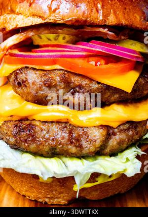 Un double cheeseburger est empilé avec de la laitue, de la tomate, de l'oignon et du fromage sur une surface en bois. Banque D'Images