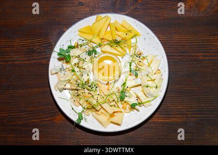 Un plateau montre différentes sortes de fromages et des tranches de fruits. Un petit bol de miel se trouve au milieu. Les légumes verts et les noix frais s'ajoutent à l'affichage. Banque D'Images