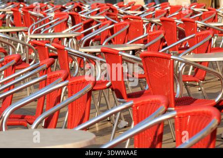 Rangées de chaises de café rouges et de tables disposées dans le coin salon extérieur, créant des motifs répétitifs dans le cadre d'une terrasse de restaurant. Banque D'Images