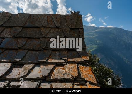 Toiture traditionnelle en ardoise d'une maison Kinnauri dans le village de Roghi avec un paysage de montagne au loin. Banque D'Images