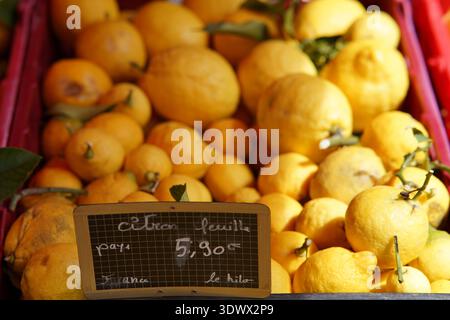 Citrons jaunes frais empilés haut avec des feuilles à l'étal du marché de Provence au prix de 2,90€/kg.Menton, France Banque D'Images