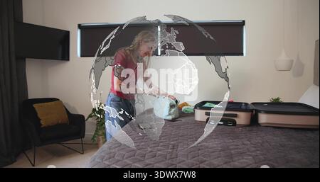 Femme d'emballage dans le haut rouge et jeans penchés sur le lit arrangeant les articles dans la valise, recouvrement globe Banque D'Images