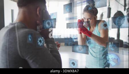 Boxeur féminin d'entraînement portant un débardeur bleu et des enveloppes rouges, entraîneur frappant dans la salle de gym avec interface utilisateur numérique Banque D'Images