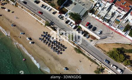 Vue aérienne de dessus de la plage de Vrahos, Grèce. Drone shot de la mer Ionienne turquoise, côte sablonneuse avec des parasols, voitures garées et route côtière en été. Banque D'Images
