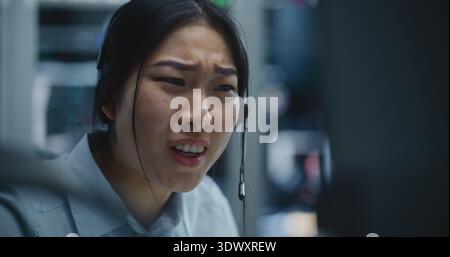 La négociante asiatique reçoit un appel via le casque tout en surveillant les données financières dans Modern Stock Office. Femme écoute Bad News à propos de la performance du marché, expression déplace l'inquiétude et la détresse. Banque D'Images