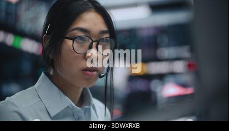 Gros plan sur une jeune femme asiatique dans le secteur des micro-casques analyse des graphiques, exécution des ordres de vente et d'achat stratégiques, gestion des stocks et des actifs numériques avec précision et confiance dans un environnement financier rapide. Banque D'Images