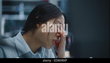 La négociante asiatique reçoit un appel via le casque tout en surveillant les données financières dans Modern Stock Office. Femme écoute Bad News à propos de la performance du marché, expression déplace l'inquiétude et la détresse. Banque D'Images
