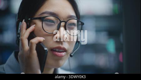 Le courtier féminin mène une conversation sur smartphone effectue des transactions d'achat et de vente sur ordinateur. En examinant les tableaux de bord financiers et en suivant les changements de marché, Girl fournit des mises à jour sur le rendement des parts de marché. Banque D'Images