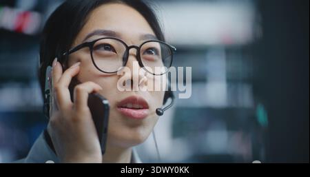 Le courtier féminin mène une conversation sur smartphone effectue des transactions d'achat et de vente sur ordinateur. En examinant les tableaux de bord financiers et en suivant les changements de marché, Girl fournit des mises à jour sur le rendement des parts de marché. Banque D'Images