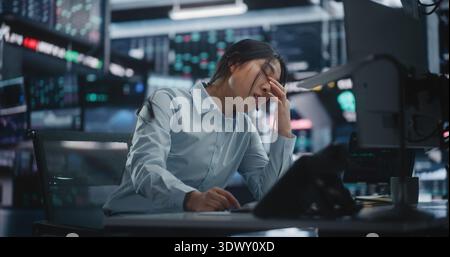 Emotional Asian Woman Broker reçoit des nouvelles dévastatrices sur le casque à propos de l'effondrement soudain du marché boursier. La femme bouleversée se dresse dans les cartes rouges de chute de panique Scan. Stress professionnel et crise financière. Banque D'Images