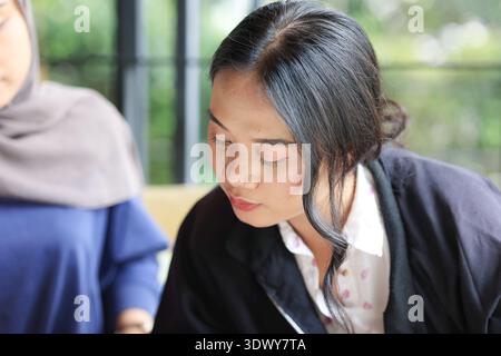 Jeune femme asiatique aux cheveux noirs se concentrant sur le travail et regardant vers le bas Banque D'Images