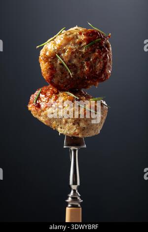 Côtelettes de porc-boeuf maison saupoudrées de romarin dans un style rustique sur un fond noir. Deux côtelettes sur une fourchette. Banque D'Images