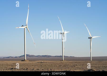 Trois éoliennes se trouvent dans un vaste désert sec avec des montagnes lointaines, générant de l'énergie renouvelable sous la lumière du soleil. Banque D'Images
