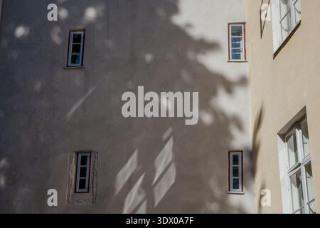 Façade d'un bâtiment historique beige à Tallinn, Estonie, avec des fenêtres à cadre blanc, des bordures rouges et des ombres d'arbres en plein soleil Banque D'Images