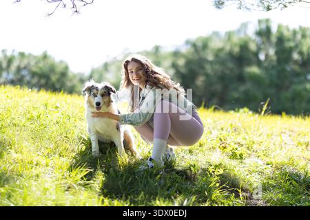 Heureuse jeune femme caressant un chien de berger australien à l'extérieur Banque D'Images