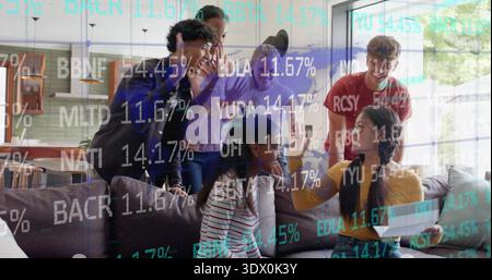 Rassemblement de six personnes se penchant autour du canapé sectionnel gris à la maison, regardant ordinateur portable avec stock ticker Banque D'Images