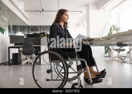 Femme d'affaires sérieuse du moyen-Orient avec la paraplégie tapant sur ordinateur portable Banque D'Images