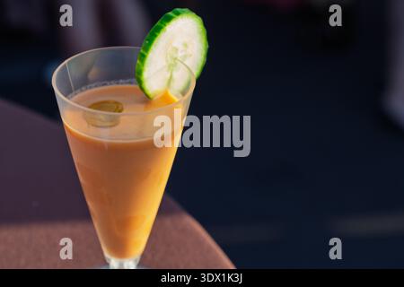 Une soupe gazpacho rafraîchissante est servie dans un verre transparent, garnie d’une tranche de concombre et d’un tourbillon d’huile d’olive. Banque D'Images
