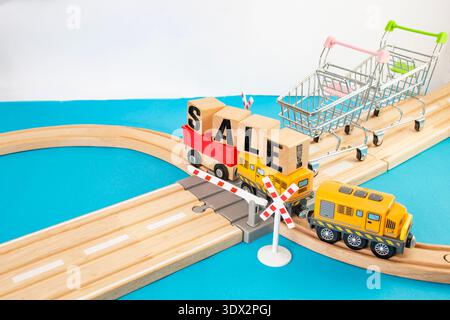 Deux chariots attendant sur un passage à niveau ferroviaire avec un train de jouets transportant des cubes en bois avec mot de vente écrit, concept commercial Banque D'Images