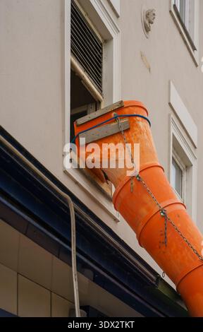 Goulotte de débris en plastique fixée avec des chaînes et du bois à la fenêtre du bâtiment résidentiel. Rénovation extérieure, travaux de réparation et détails de construction urbaine Banque D'Images