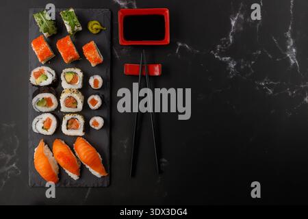 Délicieux ensemble de sushis assortis avec baguettes et sauce soja sur planche de pierre. Sushi maki avec masago, caviar, avocat, sésame, saumon, roquette. Sombre Banque D'Images