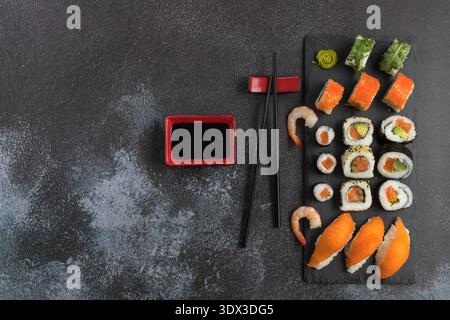 Délicieux ensemble de sushis assortis avec baguettes et sauce soja sur planche de pierre. Sushi maki avec masago, caviar, avocat, sésame, saumon, roquette. Sombre Banque D'Images